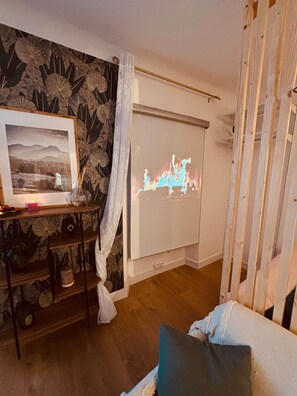 A room with a projector screen displaying a fire animation, a framed photograph on a shelf, and a wooden floor.