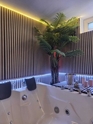 A modern bathroom with a large bathtub, a potted palm plant, and a striped wall design.