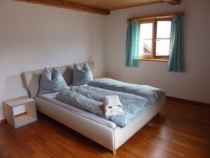 Une chambre à coucher avec un lit, un plancher en bois et une fenêtre avec des rideaux.