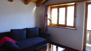 Una sala de estar con un sofá azul oscuro, una mesa de centro de vidrio y una ventana con cortinas.