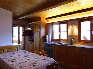 A cozy kitchen with wooden cabinets, a dining table with a patterned tablecloth, and a hanging pendant light. - Jassa Sura, (Tschlin). by Interhome (Tschlin)