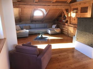 A loft-style room with a wooden ceiling, a glass ceiling window, a sofa, a coffee table, and a kitchen area with wooden cabinets. - Jassa Sura, (Tschlin). by Interhome (Tschlin)