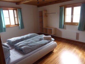 Une pièce comprenant un lit, un plancher en bois, une fenêtre avec des rideaux et une étagère intégrée.