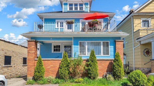 Une maison à deux étages avec un balcon, un parasol rouge et une cheminée en briques.