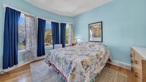 Une chambre à coucher avec un lit, une fenêtre avec des rideaux, une table de chevet, une lampe et un tableau au mur.