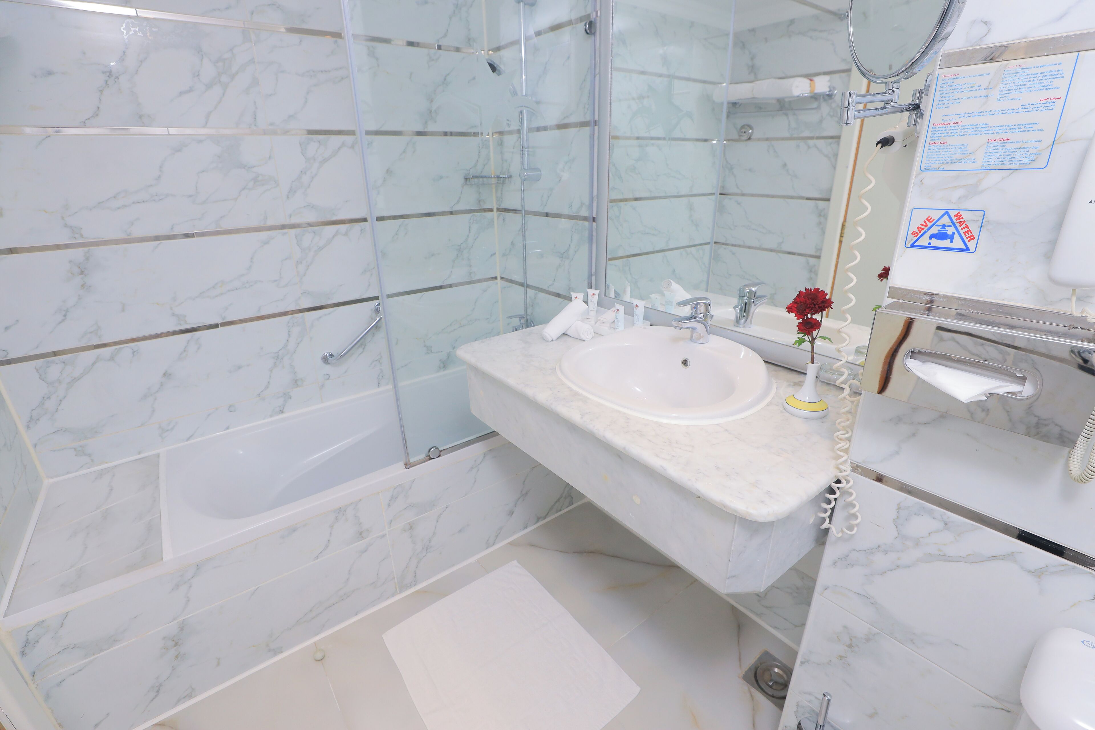 Un baño con lavamanos de mármol, ducha y espejo con señal de seguridad.