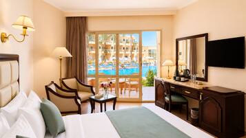A hotel room with a bed, desk, chairs, a TV, and a view of a pool and buildings.