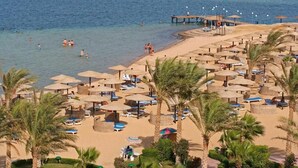 Un resort en la playa con sombrillas, sillones de descanso y un muelle que se adentra en el agua.