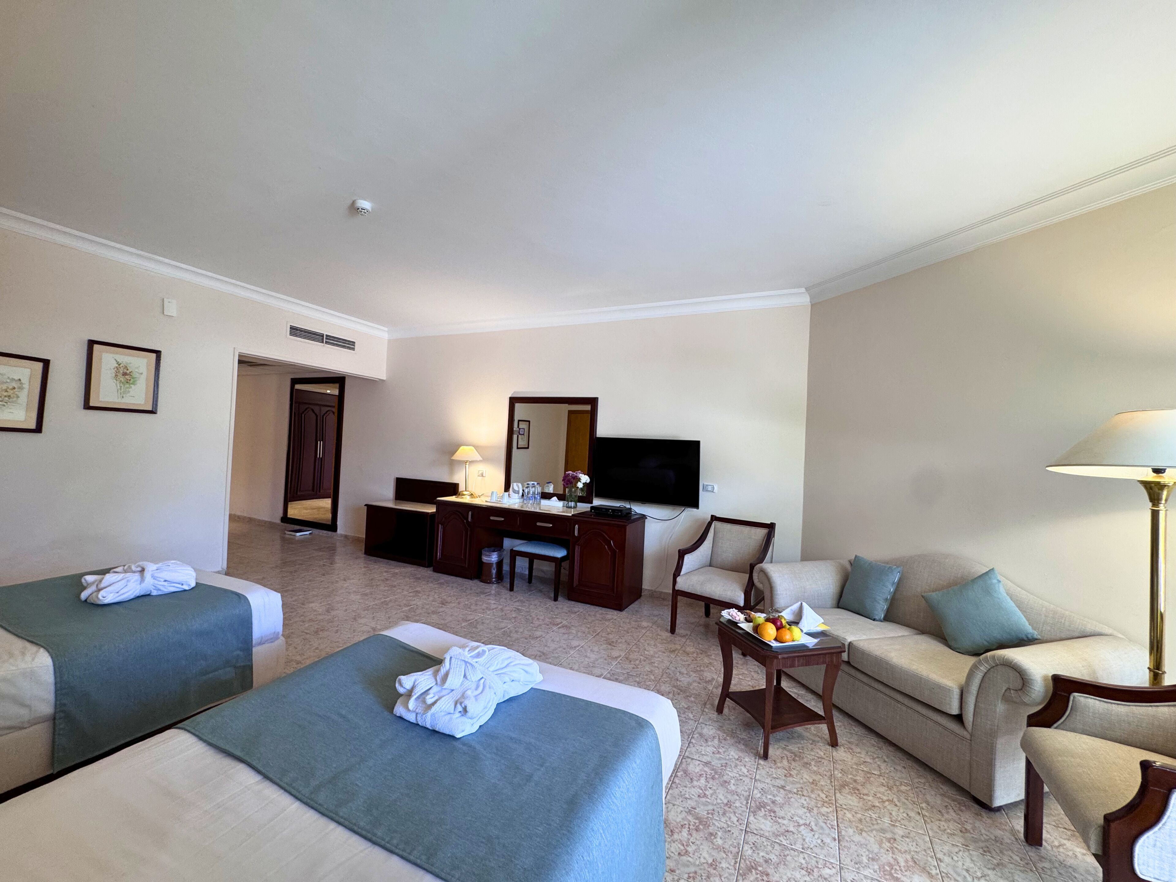 Ein Hotelzimmer mit zwei Betten, einem Schreibtisch, einem Sessel, einer Couch und einem Fernseher.