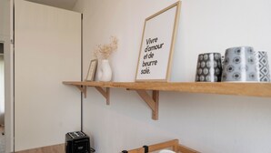 A kitchen area with a wooden shelf holding a framed inspirational quote, a white vase with dried flowers, and patterned mugs.