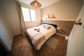 A bedroom with a bed, a window, a radiator, a wooden floor, and a wall-mounted shelf with pictures. - Bright T3 with balcony and parking, 6 pers, Procé (Nantes)