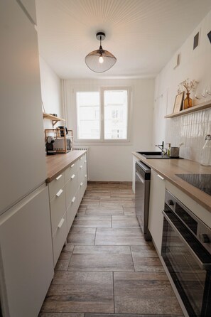 Una cocina estrecha con armarios blancos, encimera de madera, horno empotrado y ventana con persianas.