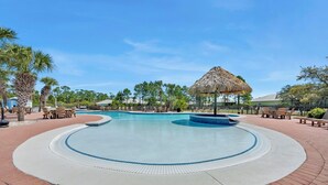 Ein Swimmingpool mit einem strohgedeckten Pavillon, umgeben von Palmen und Liegestühlen.