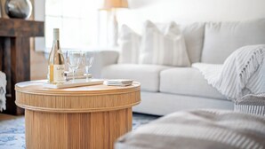 Ein runder Holztisch mit einer Flasche und Gläsern, ein weißes Sofa und eine Lampe in einem Wohnzimmer.
