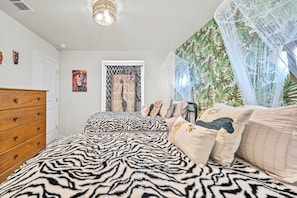 Ein Schlafzimmer mit einer bettenwaiderme aus Zebramuster, einem hölzernen Schminktisch, einem an der Wand befestigten Zebra-Kopf-Dekoration, einem gerahmten Kunstwerk und einem gemusterten Vorhang.