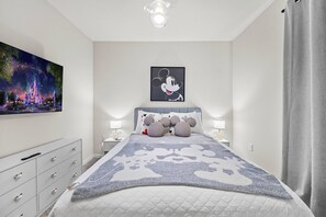 Ein Schlafzimmer mit einem großen Bett, einem Nachttisch, einer Kommode, einem an der Wand hängenden Bild und einem Fenster mit Vorhängen.