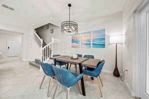 Ein Essbereich mit einem Holztisch, blauen Stühlen, einer Chandelüster und einer Treppe.