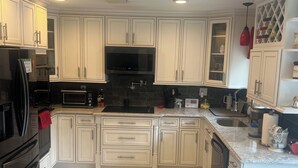 A modern kitchen with white cabinetry, a black microwave, and a stainless steel refrigerator.