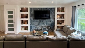 Un soggiorno moderno con una grande TV a schermo piatto montata su una parete in marmo, un divano componibile e scaffali a parete con oggetti decorativi.