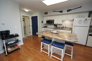A compact kitchen with white cabinets, a granite countertop, two bar stools, a microwave, a stove, and a refrigerator. - Stay Here, Boat There- Walk to Jet + Pool & Beach (Port Clinton)