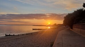 A sunset over a calm body of water with a promenade and distant city skyline.