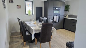 A dining area with a table set for four, a modern kitchen with an oven, and a window with blinds.