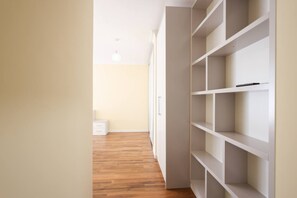 Un couloir doté d’un plancher en bois qui mène à un placard blanc muni de plusieurs étagères.