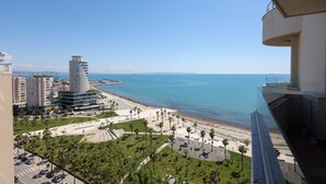 Un paisaje costero con un edificio moderno destacado, un paseo marítimo frente a la playa y una vista despejada del mar.