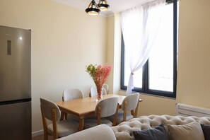 A dining area with a table, chairs, a vase with flowers, a sofa, and a window with curtains. - Panoramic Sea-View Apartment, Durrës Promenade (Durrës)