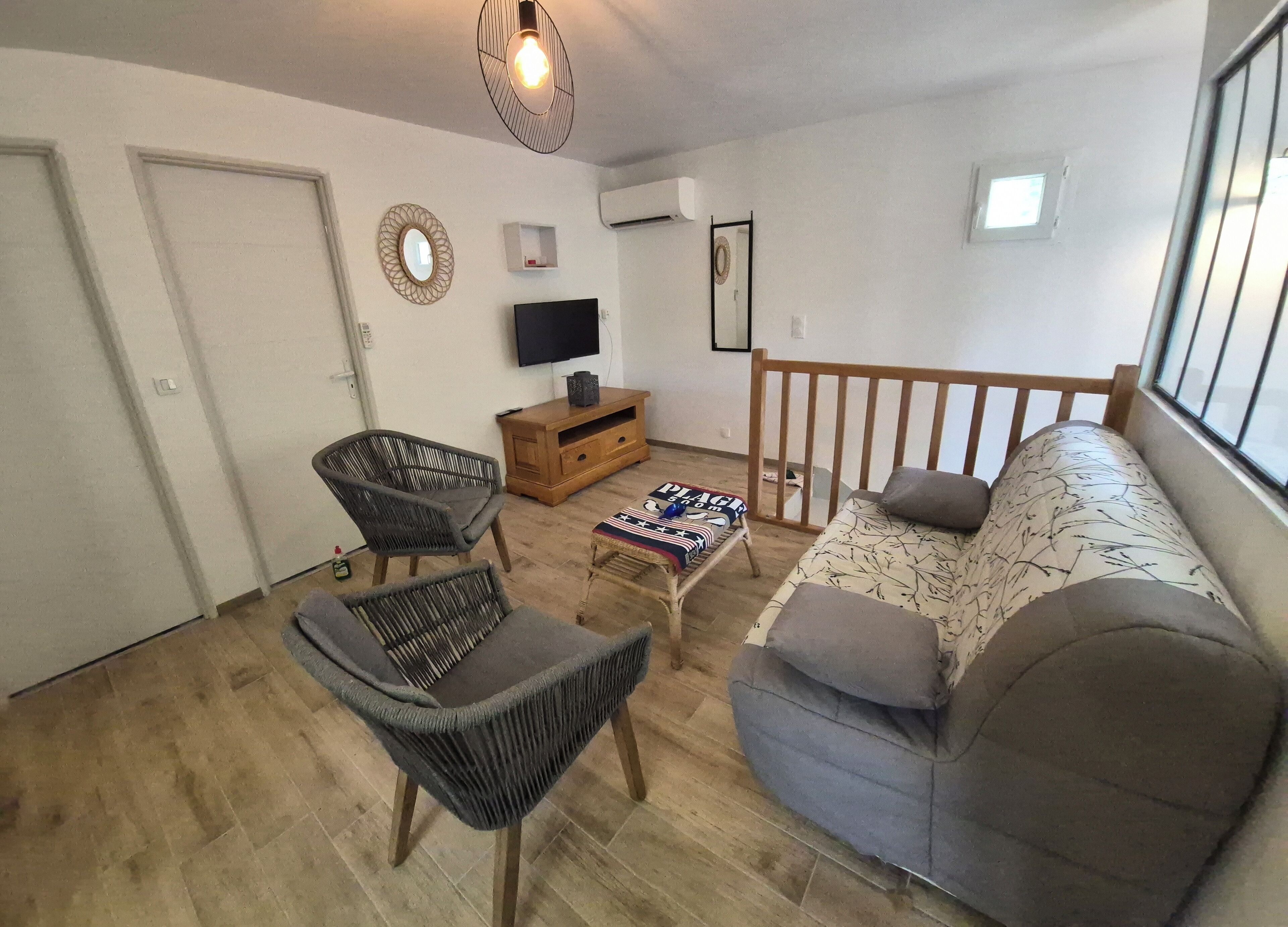 A living room with a sofa, two chairs, a TV, a wooden cabinet, and a small table with a blanket.