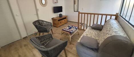 A living room with a sofa, two chairs, a TV, a wooden cabinet, and a small table with a blanket.