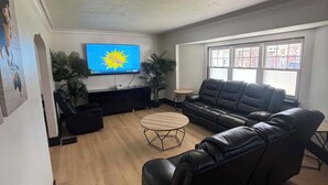 A living room with a black leather sofa, a wooden coffee table, and a TV mounted on the wall.