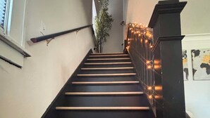 A staircase with wooden steps and black railings, leading to a landing with a plant and string lights.