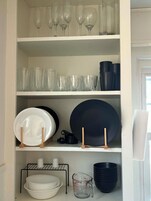 Un estante de cocina con copas de vino, vasos transparentes, platos, tazones y tazas medidoras.