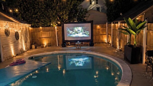 A backyard with a swimming pool, a wooden fence, and a large screen for outdoor viewing.