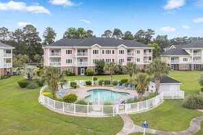 Ein mehrstöckiges Hotel mit Swimmingpool, umgeben von Palmen und Liegestühlen.