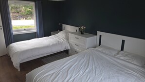 Habitación de hotel con dos camas, una ventana con cortinas, una mesita de noche con un jarrón de flores y otra mesita junto a la cama.
