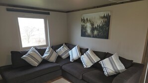 Un sofá modular con almohadones a rayas, una ventana y un cuadro con motivos forestales en la pared.