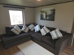 Um sofá modular com almofadas listradas, uma janela e uma pintura com tema de floresta na parede.