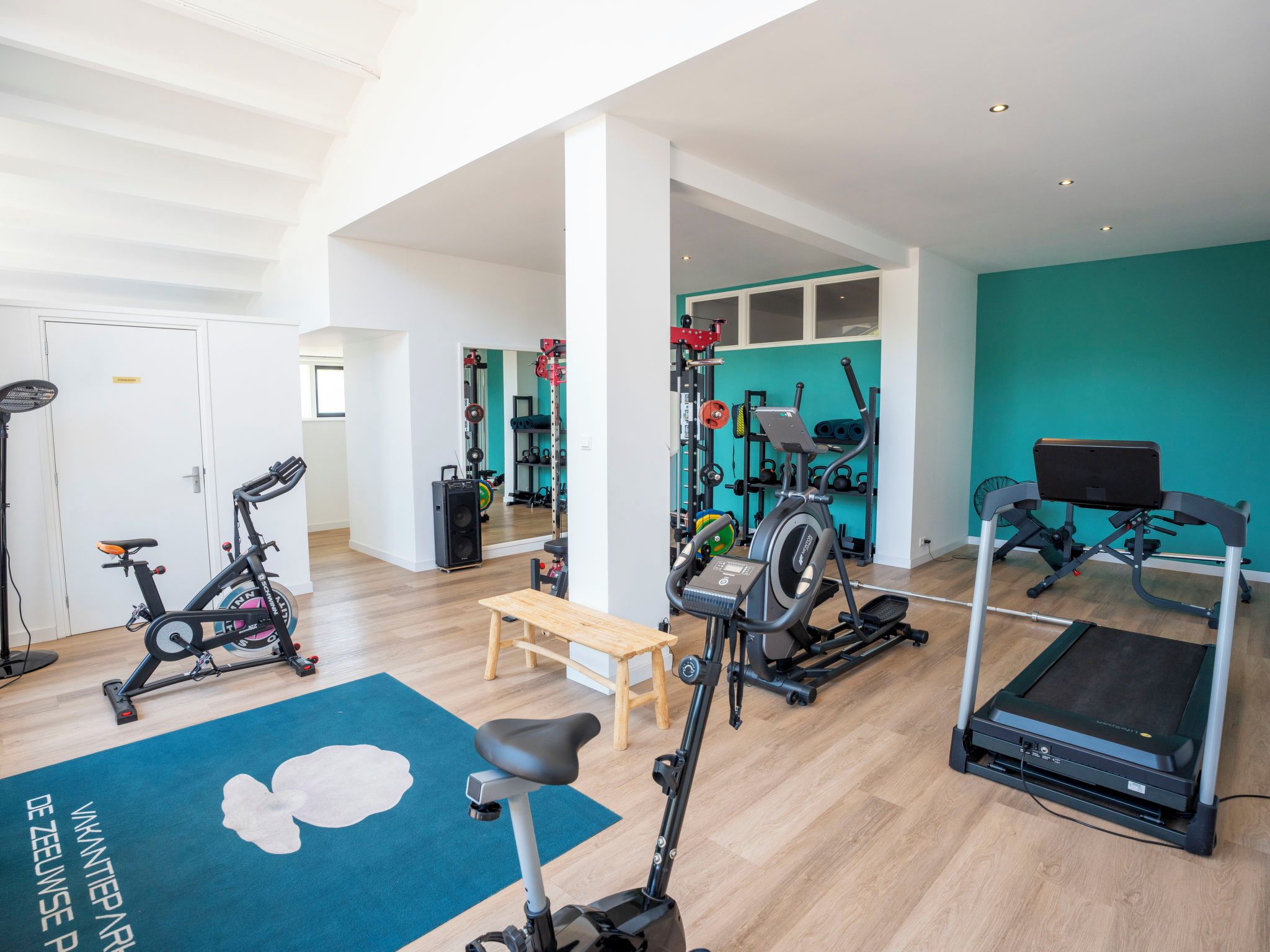 A spacious indoor gym with various exercise equipment, a wooden bench, and a blue exercise mat.
