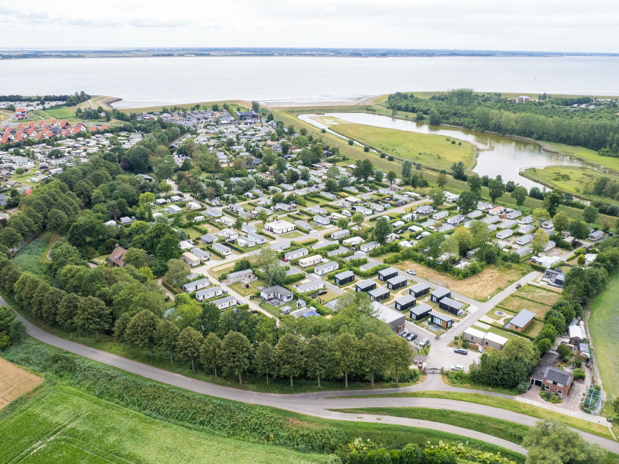 An aerial view of a residential area with houses arranged in a grid pattern, surrounded by greenery and a body of water.