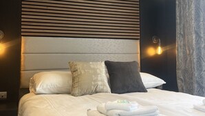 Una habitación de hotel moderna con una cama grande, dos almohadas, un cabecero con líneas horizontales y apliques de pared.