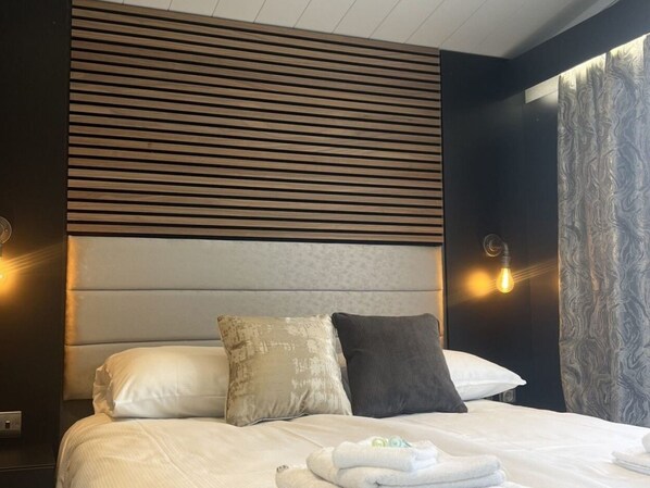 Una habitación de hotel moderna con una cama grande, dos almohadas, un cabecero con líneas horizontales y apliques de pared.