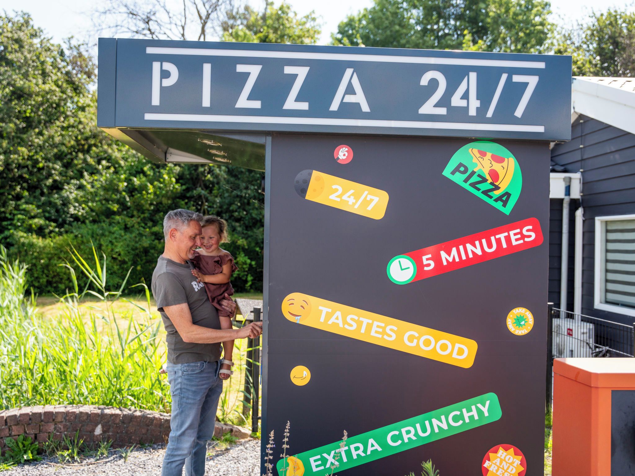 Letrero de una pizzería que ofrece servicio las 24 horas, entrega en 5 minutos, y destaca que la pizza es deliciosa y extra crujiente.
