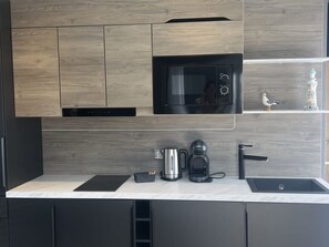 Una cocina moderna con microondas integrado, cafetera y un lavamanos pequeño.
