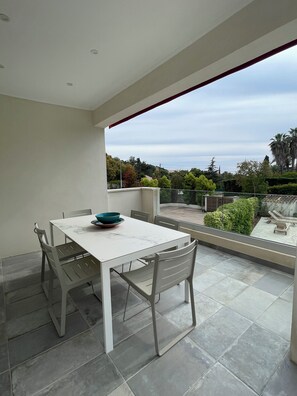 A modern outdoor dining area with a white table and chairs, a teal bowl, and a view of a landscaped garden and distant buildings. - Contemporary Villa & Pool (Ajaccio)
