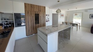 Cuina moderna amb una illa central, armaris de fusta i zona de menjador amb taula i cadires.