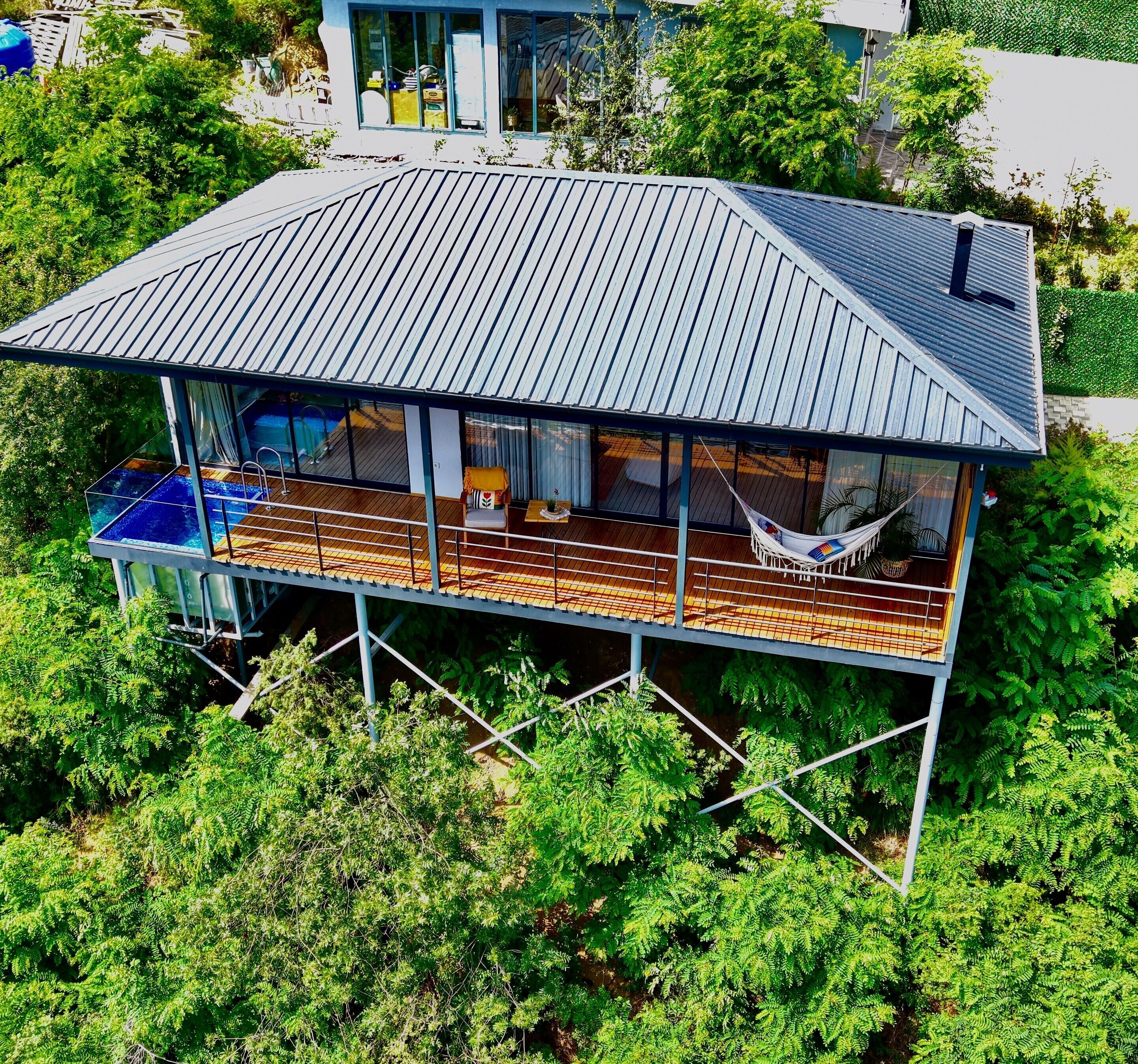 A modern house with a large deck, a hammock, and a swimming pool.