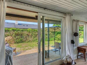 Ein Zimmer mit einer Schiebeglastür, die auf eine Terrasse mit einem Stuhl und Sonnenschirm führt.