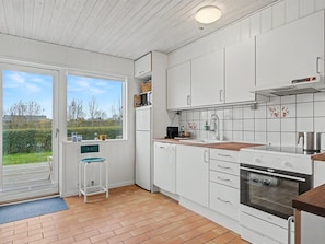 A modern kitchen with white cabinets, a built-in oven, and a large window offering a view of the outdoors. - "Jarik" - 340m from the sea by Interhome (Bogense)